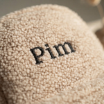 Een haarscherpe macro close-up van de zwarte borduurnaam 'Pim' op de pluizige beige teddy stof van de rugzak.