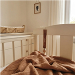 Het cognac velvet speenkoord met witte borduring 'Sepp' hangend aan de spijlen van een wit houten ledikantje in een sfeervolle kinderkamer.