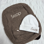 Een kraamcadeau voor Sepp bestaande uit een taupe kleurige kinderrugzak met naam gepersonaliseerd en witte kindermuts. 